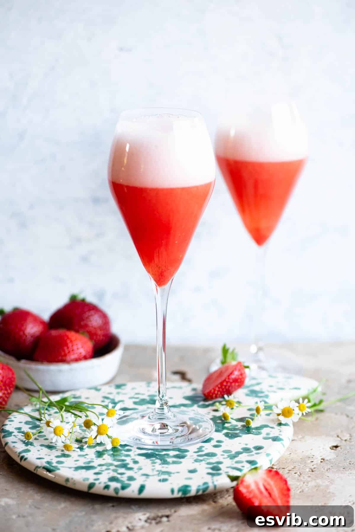Two elegant flute glasses filled with vibrant Rossini cocktails (Strawberry Bellinis), ready to be enjoyed on a stone counter with a soft blue background, evoking a sense of celebration.