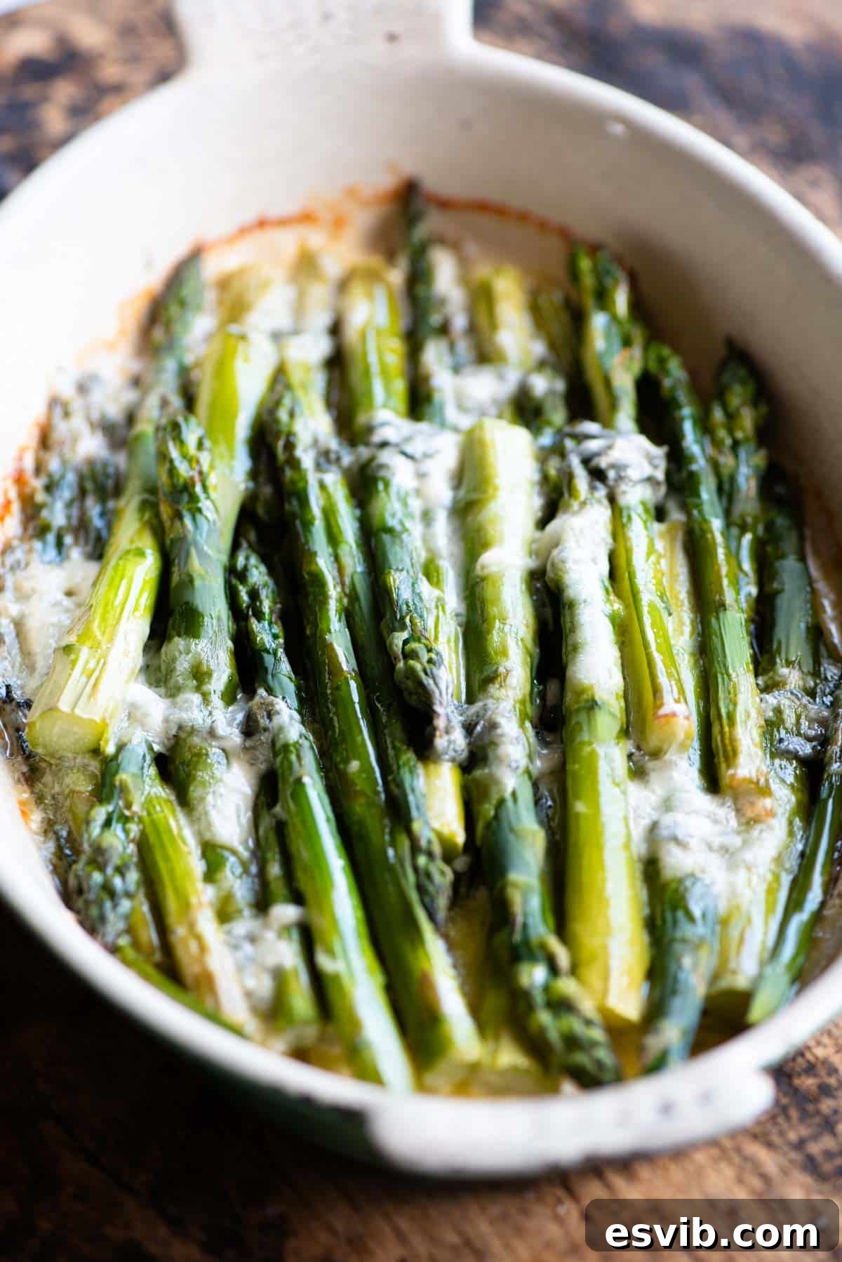 A side shot of roasted asparagus in an oval baking dish topped with gorgonzola, showcasing the melted cheese and tender spears.