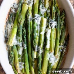 A cropped square image of roasted asparagus in a baking dish topped with gorgonzola cheese, inviting you to taste.