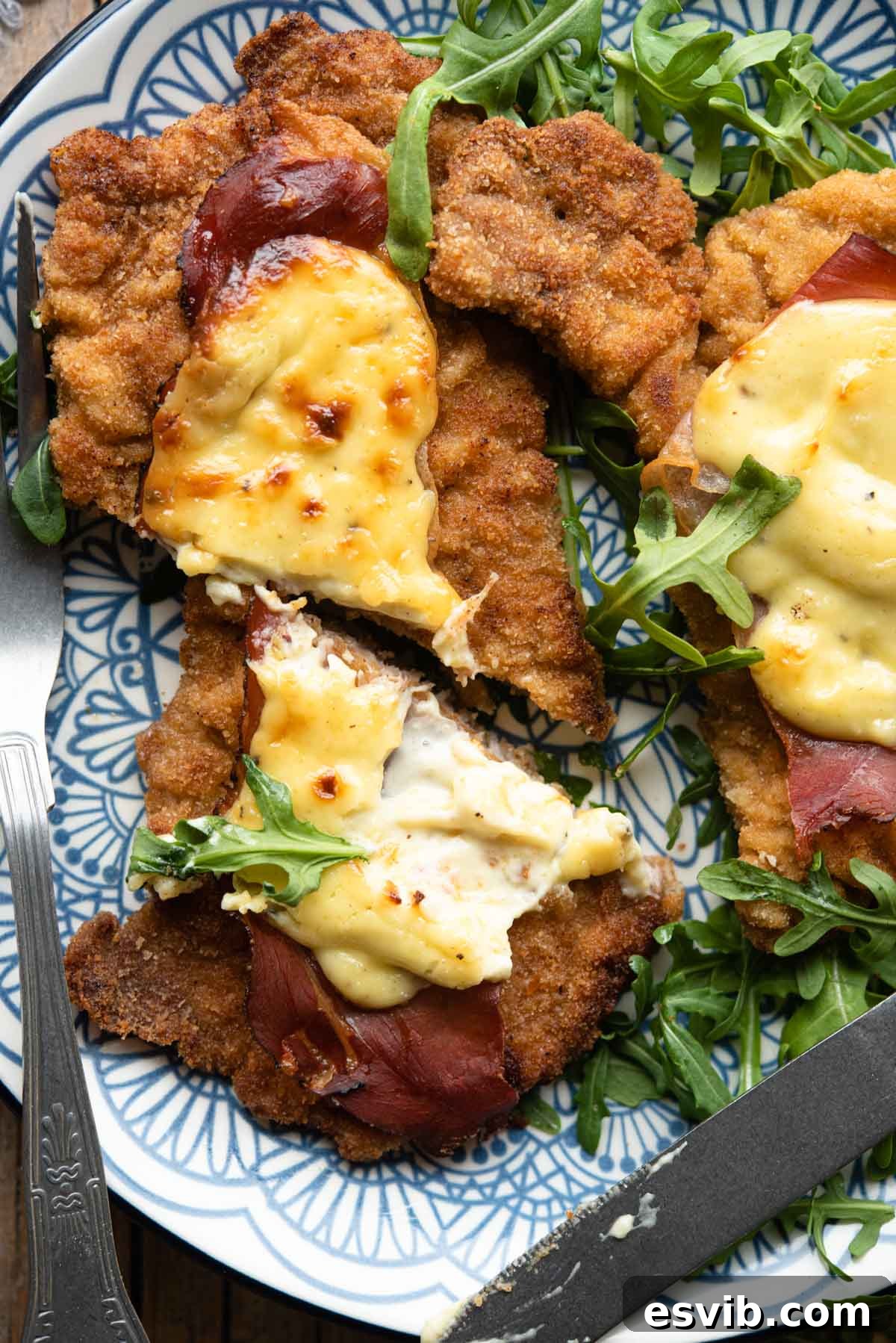 Crispy Veal with Creamy Parmesan Sauce 2 A close up of a veal cutlet cut in half with parmesan cream and prosciutto on top, showcasing its delicious layers and golden crust.