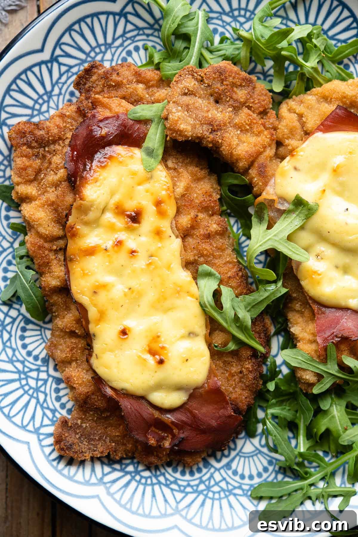 Crispy Veal with Creamy Parmesan Sauce 7 An overhead shot of exquisite breaded veal cutlets on a serving plate, generously topped with creamy parmesan sauce and crispy prosciutto, garnished and ready to serve.