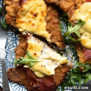 A close up of a veal cutlet cut in half topped with prosciutto and parmesan cream, ready to serve.