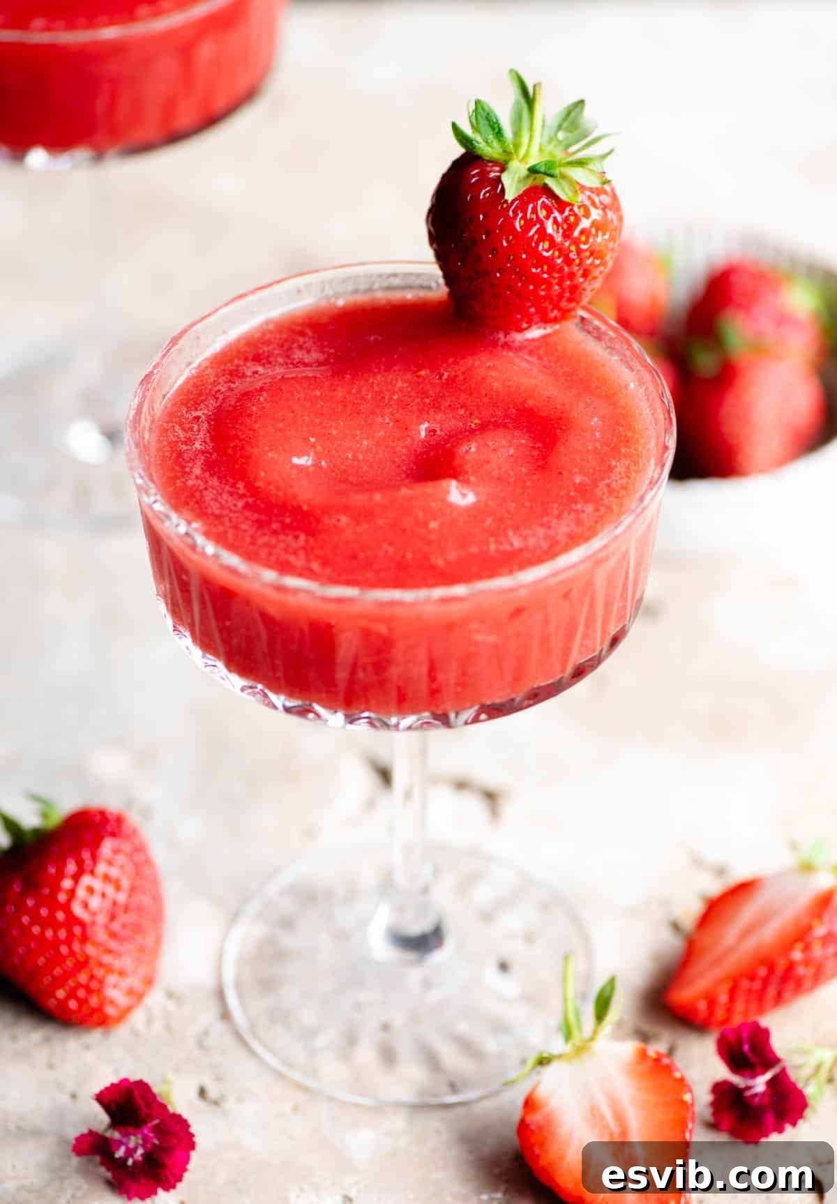 Strawberry Velvet Fizz 3 A close up shot of a luxurious frozen strawberry cocktail in a delicate cocktail glass, beautifully garnished with a single fresh strawberry, emphasizing its icy and inviting texture.