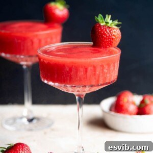 A close-up view of a vibrant frozen strawberry cocktail in a glass, garnished with a whole, fresh strawberry, highlighting its irresistible texture.