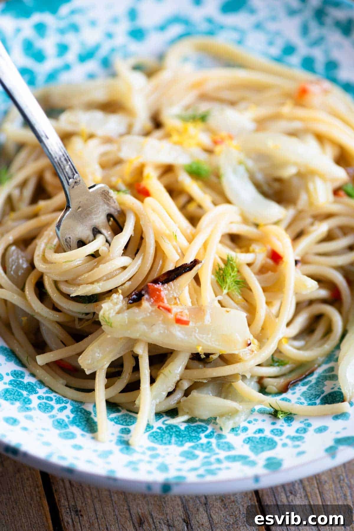 Smoky Fennel Pasta with Citrus Spice 6 A close up of roasted fennel spaghetti in a blue bowl, twirled around a fork, showcasing the vibrant ingredients.