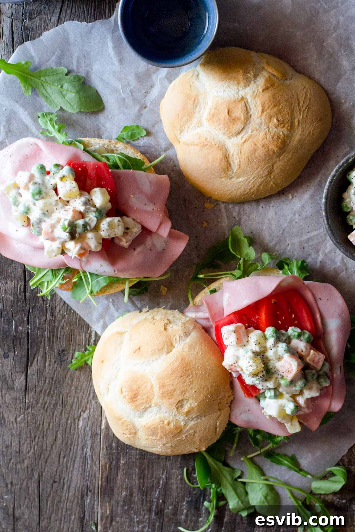 An overhead shot of creamy Russian Salad served on two rustic bread rolls, garnished lightly.