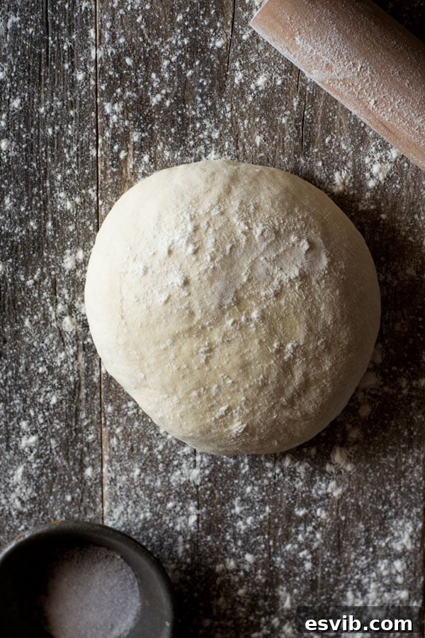 An overhead shot showcasing a ball of yeast-free pizza dough on a floured wooden surface.