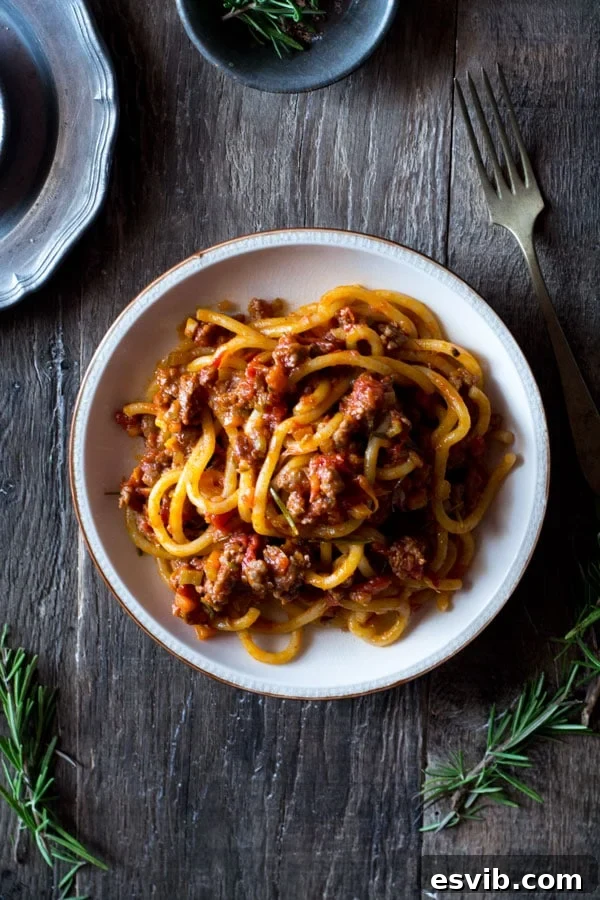 Pici pasta served with a rich Tuscan sausage ragu, featuring crumbled Italian sausage, vibrant tomato sauce, and fresh herbs in a rustic kitchen setting.