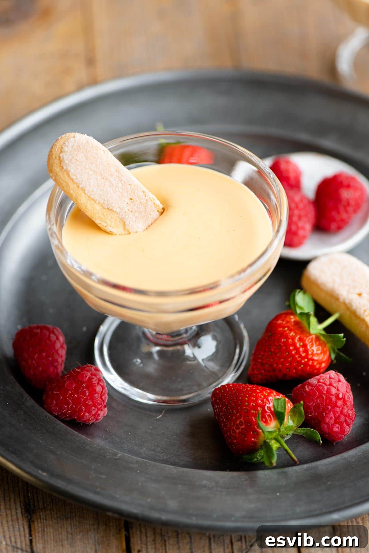 Silky Italian Zabaglione Delight 2 A small glass bowl filled with golden Zabaglione, featuring a savoiardi cookie gracefully dipped into its creamy texture