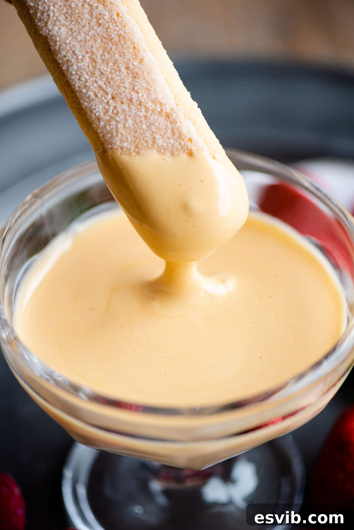 Silky Italian Zabaglione Delight 5 A close up of a savoiardi cookie being dunked into golden, frothy Zabaglione in a glass bowl.