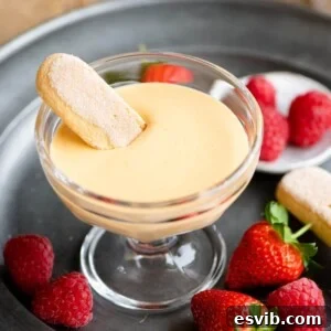 Zabaglione in a glass serving dish with a savoiardi biscuit dunked in and berries at the side