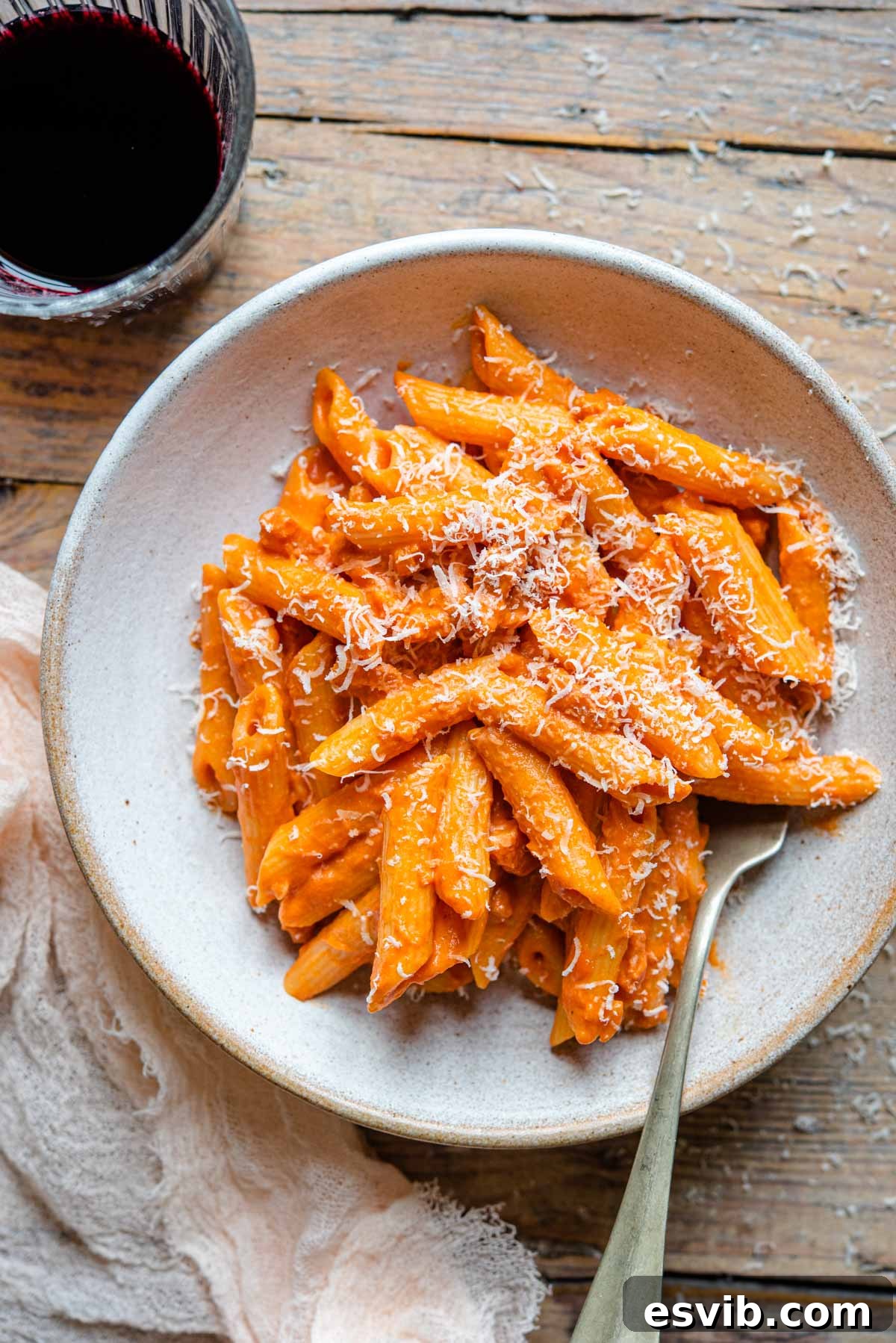 An overhead shot of penne alla vodka in a rustic bowl with a glass of red wine at the side, showcasing the creamy texture and rich color of the sauce