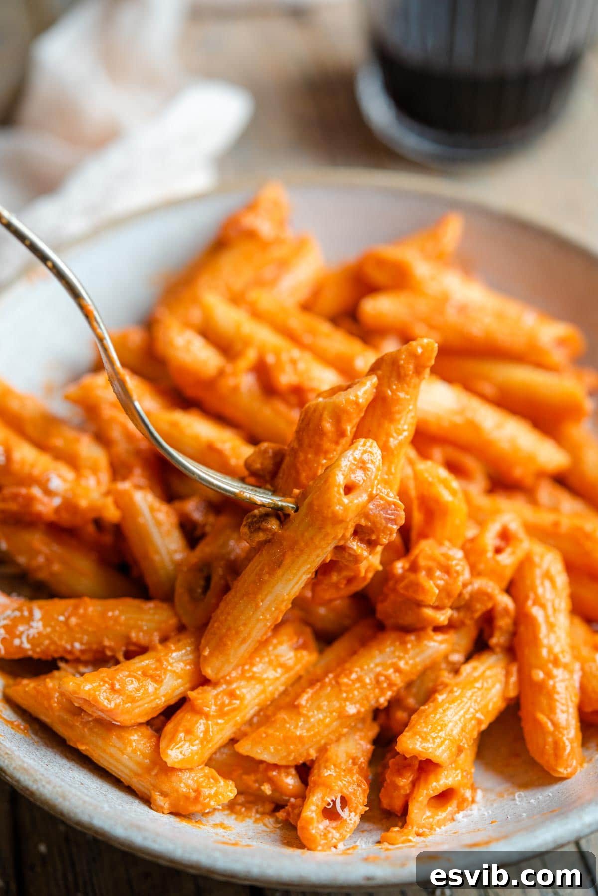 A close up of a fork picking up penne alla vodka, showing the creamy tomato sauce clinging to the pasta
