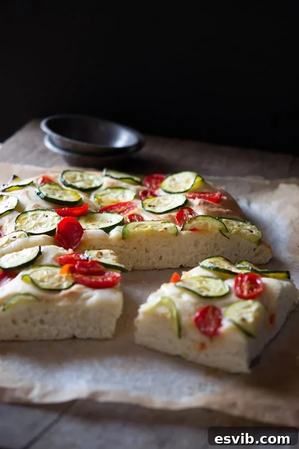 Delicious zucchini tomato focaccia. A simple Italian snack or appetizer with a crispy crust and soft, light and fluffy middle. Authentic Italian recipes and traditional Italian recipes at Inside the rustic kitchen. Freshly baked zucchini tomato focaccia with a crispy crust and soft, light and fluffy middle. Garnished with basil, at Inside the rustic kitchen.