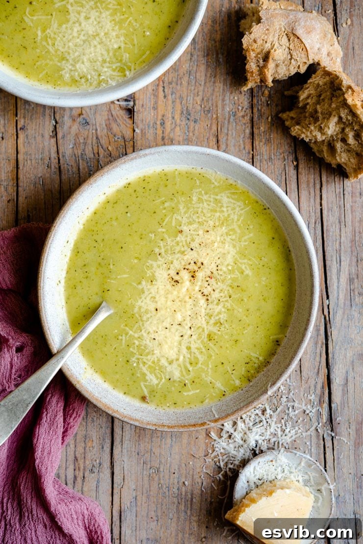 An overhead shot of creamy zucchini soup in two bowl with crusty bread at the side