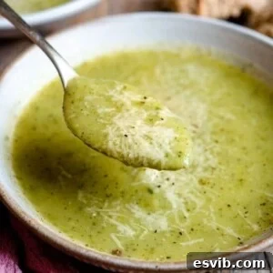 A close up of a spoonful of zucchini potato soup topped with parmesan.
