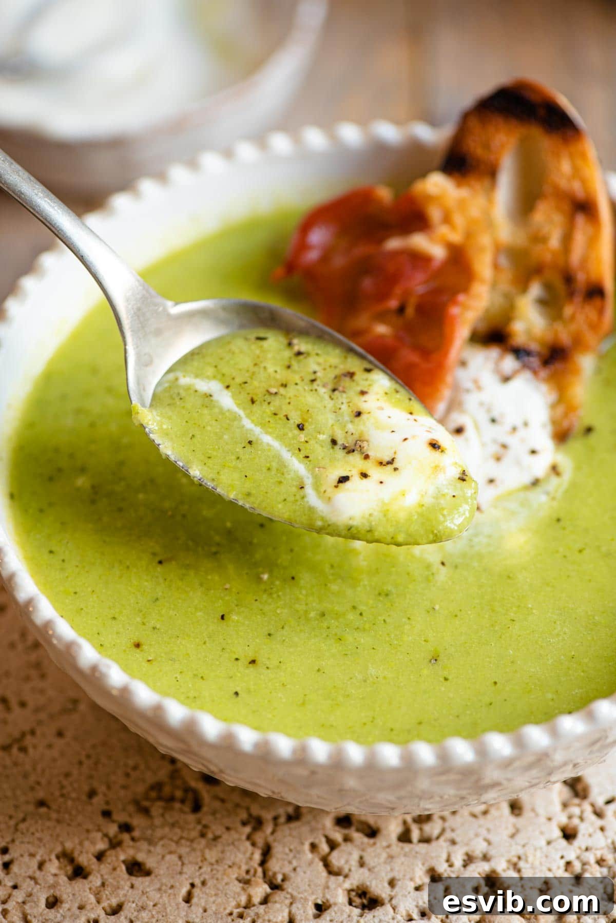 Silky Spring Pea Soup Crowned with Crispy Prosciutto 6 A close-up shot of a spoonful of creamy green pea soup, highlighting its smooth, velvety texture and vibrant green color, ready to be enjoyed as a comforting and healthy meal.
