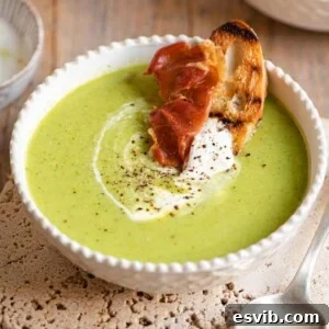 A close up of green pea soup with a slice of bread and prosciutto at the side, presenting a full and inviting meal.