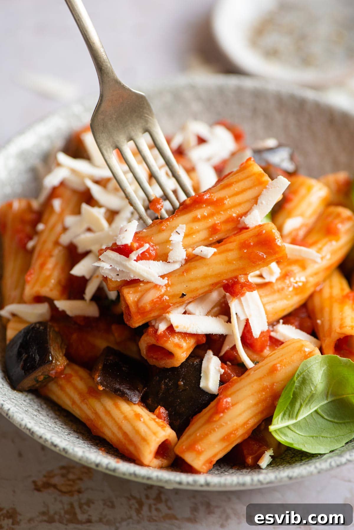 A close-up shot of a fork twirling strands of Pasta alla Norma, highlighting the tender eggplant, vibrant tomato sauce, and grated cheese.