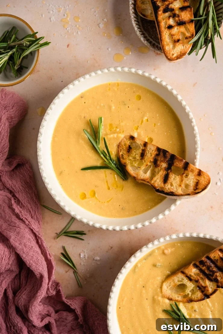 A steaming bowl of Tuscan Chickpea Soup, garnished with fresh rosemary and served with crusty ciabatta bread