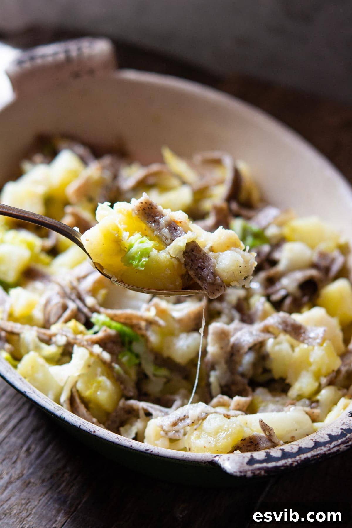 A close-up of a spoonful of steaming Pizzoccheri pasta, rich with potatoes, cabbage, and glistening melted cheese