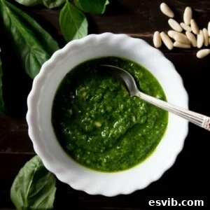 A vibrant green bowl of basil pesto, ready to be used in various dishes, with fresh basil and pine nuts scattered around.