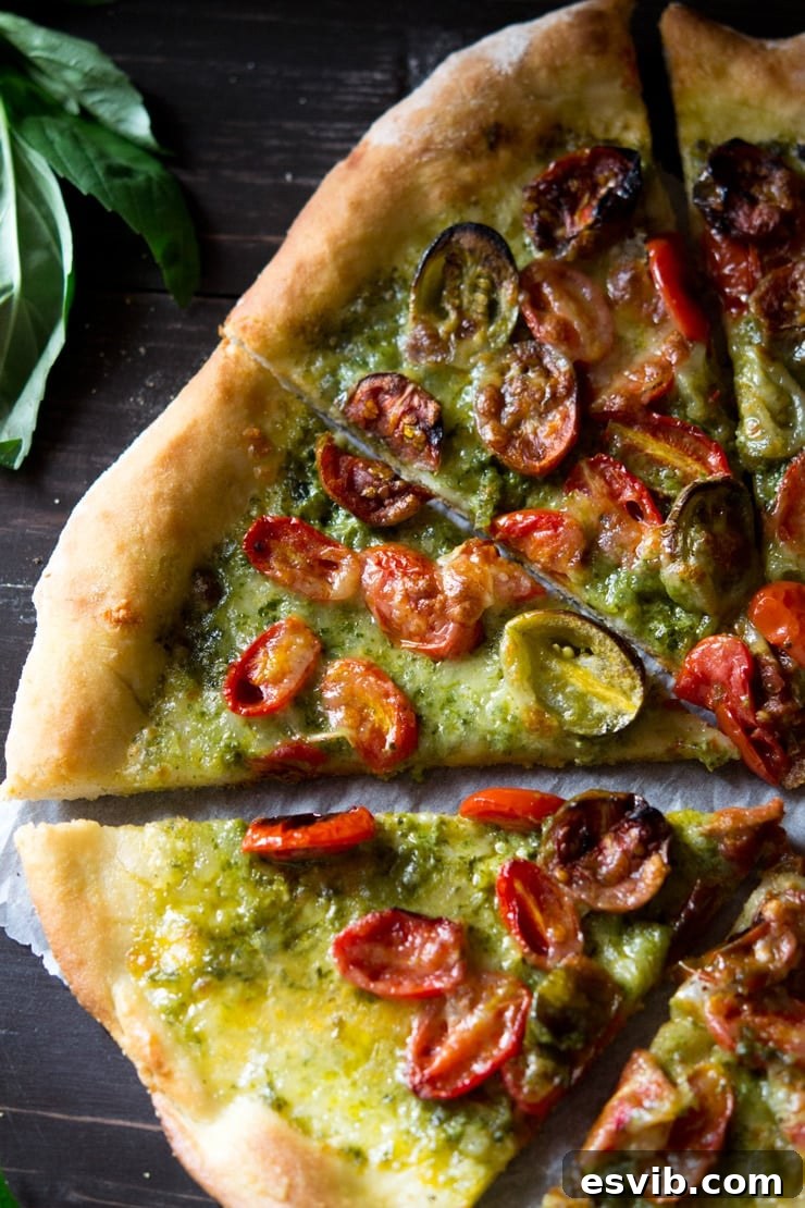 A close-up shot of a single slice of basil pesto pizza with fresh basil leaves in the background, showcasing the melted mozzarella and roasted tomatoes.