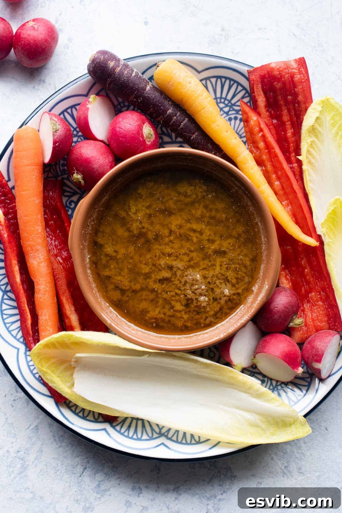 Bagna Cauda Warm Anchovy Garlic and Butter Dip 2 An overhead shot of Bagna Cauda, a warm garlic and anchovy dip, served in a traditional terracotta fujot dish with a tealight, surrounded by a vibrant assortment of raw seasonal vegetables like carrots, radishes, radicchio, and celery, all ready for dipping.