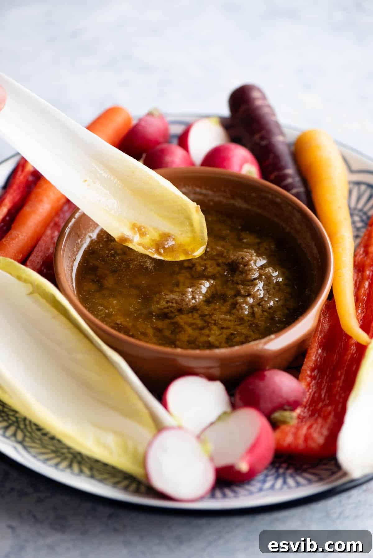 Bagna Cauda Warm Anchovy Garlic and Butter Dip 5 A close-up shot of a piece of crisp, green chicory being gently dipped into a traditional terracotta bowl filled with warm, golden Bagna Cauda, highlighting the appealing texture and inviting nature of the dip.