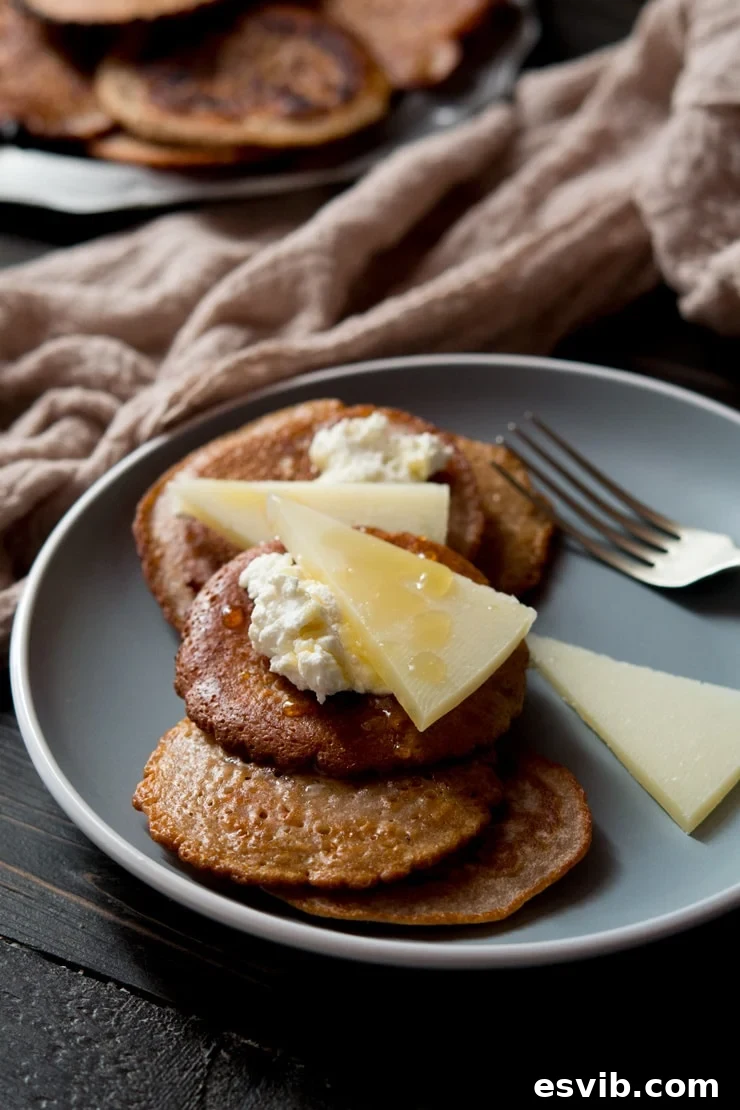 Chestnut Fritters with Ricotta, Pecorino, and Truffle Honey Warm chestnut fritters topped with creamy ricotta, slices of salty pecorino cheese, and drizzled with golden truffle honey, presented on an elegant blue plate.