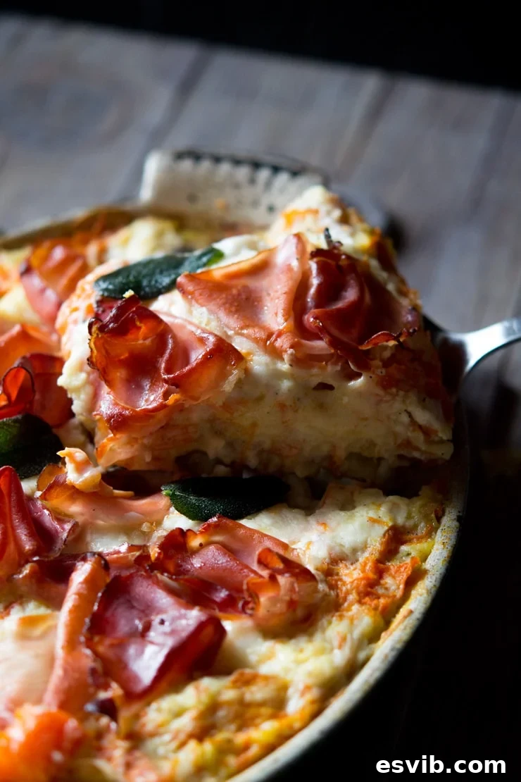 A close-up shot of a perfectly sliced piece of butternut squash lasagna, showing the layers of pasta and filling, topped with crispy prosciutto.