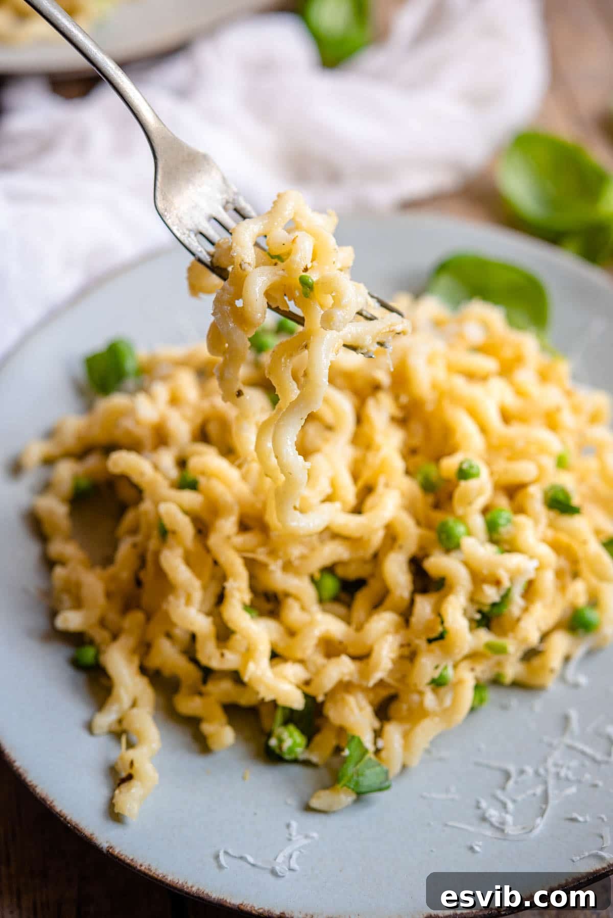 A close up of long fusilli pasta with artichokes, peas and pea shoots on a plate Close-up of Artichoke Pasta on a fork, highlighting its creamy texture