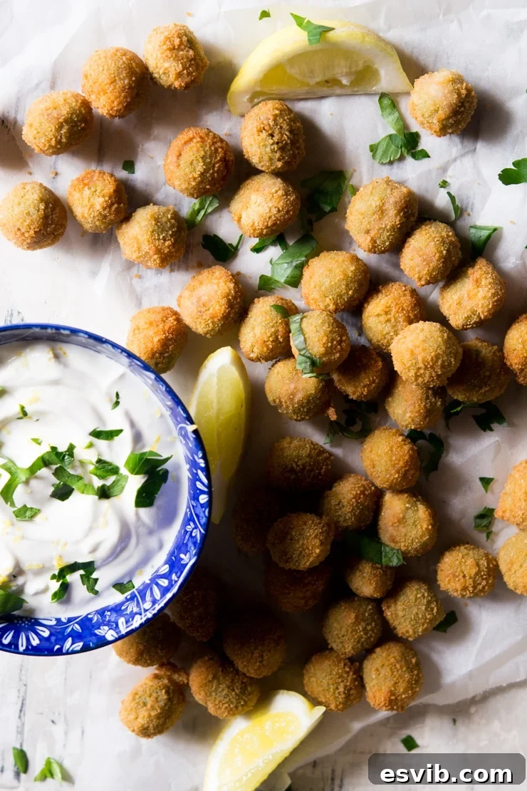 An overhead shot of fried stuffed olives and a sour cream dip, garnished with fresh herbs