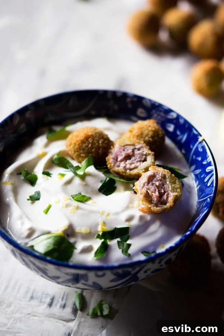 Sausage stuffed olives cut in half and placed on top of a sour cream dip, garnished with fresh herbs