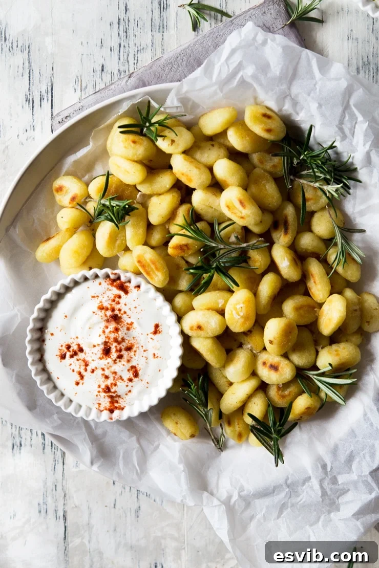 Crispy Pan-Fried Gnocchi with Rosemary and Dip An overhead shot of crispy pan-fried gnocchi with fresh rosemary on a plate, served with a creamy dip on the side