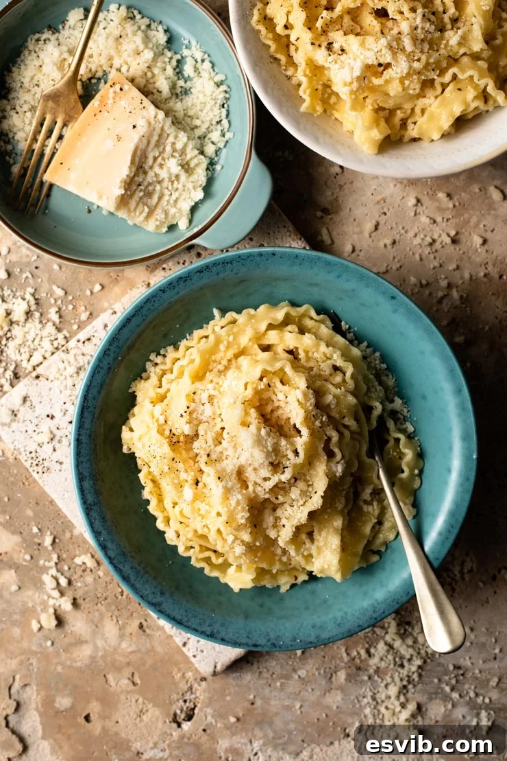 Butter Parmesan Pasta - Mafalde pasta with butter and parmesan cheese. This recipe is incredibly easy and is perfect cheesy comfort food. Four ingredient pasta recipe ready in 15 minutes. #parmesan #Italianpasta An overhead shot of two bowls of parmesan pasta with grated parmesan in a bowl at the side, highlighting its cheesy comfort.