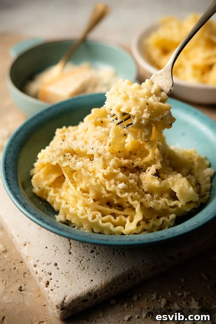 Butter Parmesan Pasta - Mafalde pasta with butter and parmesan cheese. This recipe is incredibly easy and is perfect cheesy comfort food. Four ingredient pasta recipe ready in 15 minutes. #parmesan #Italianpasta A fork picking up some parmesan pasta from a bowl, showcasing the creamy texture and cheese bits.