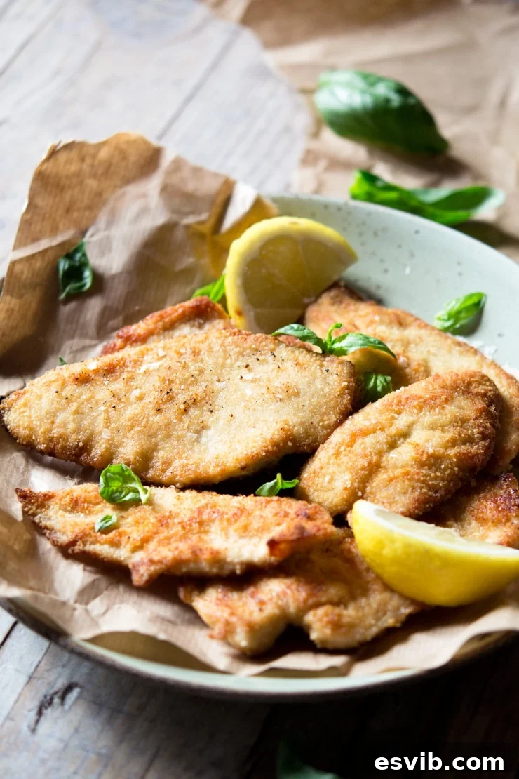 A beautiful side shot of golden breaded chicken cutlets arranged artfully on a plate, accompanied by vibrant lemon wedges, emphasizing their crispy texture.