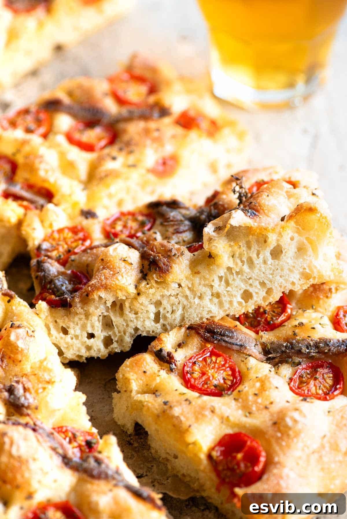 A close up of a perfectly baked slice of tomato and anchovy focaccia, presented on its side, revealing the incredibly airy and bubbly texture of the bread's interior.