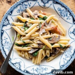 A cropped close up of mushroom spinach pasta in a blue and white bowl with a fork at the side.