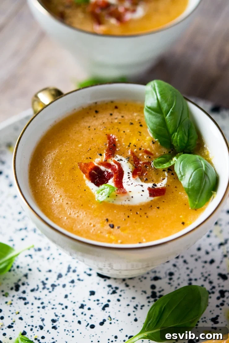 A close up of melon gazpacho soup in a mug topped with creamy yogurt and crispy prosciutto pieces