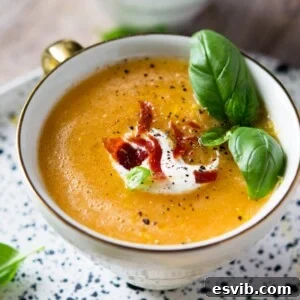 A close up of melon gazpacho in a mug topped with creme fraiche, crispy bacon and basil