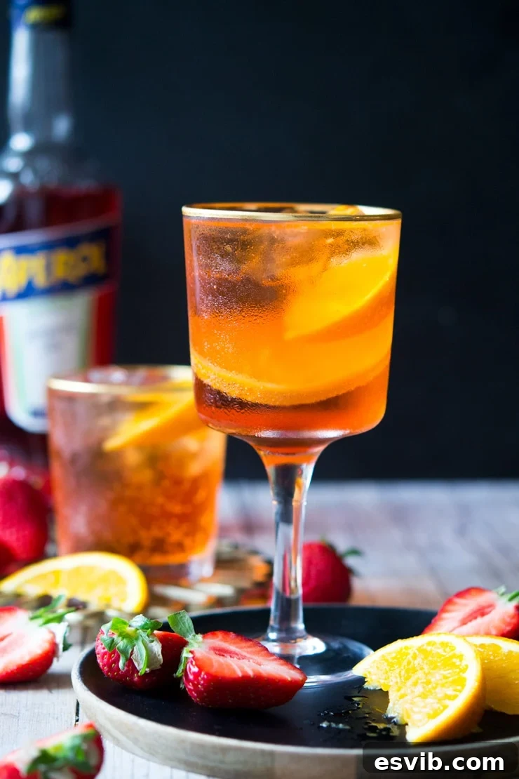 A wine glass filled with and Aperol spritz cocktail with a black background and chopped strawberries scattered around A wine glass filled with an Aperol spritz cocktail with a black background and chopped strawberries scattered around