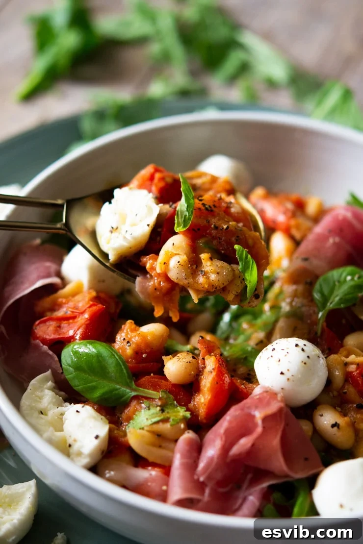 A close-up of a portion of warm white bean salad with vibrant tomato pieces, served elegantly on a white serving spoon, highlighting the textures and rich colors.