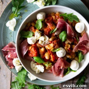 An overhead shot of a warm white bean salad in a white bowl, garnished with prosciutto and mozzarella.