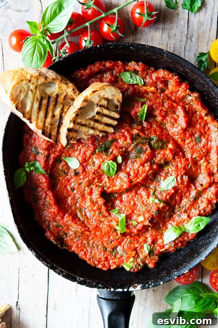A vibrant Italian tomato sauce in a saucepan, ready to be served, with two slices of char-grilled ciabatta bread nearby.