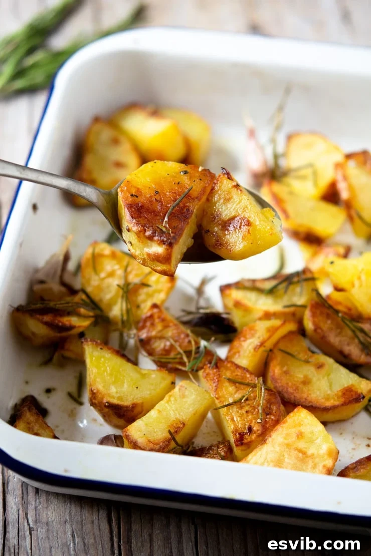 Italian Rosemary Garlic Roast Potatoes 3 A serving spoon scooping up crispy Italian roast potatoes from a baking tray, highlighting their golden brown color and texture