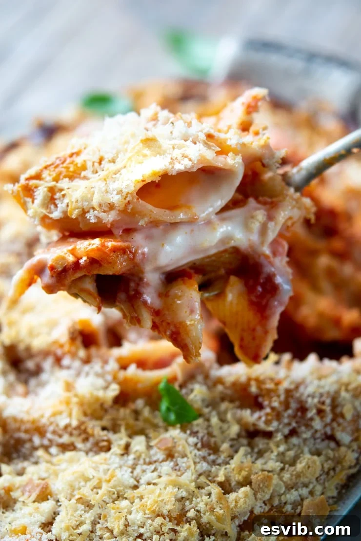 A close up of a spoon holding some oven baked pasta with cheese oozing, highlighting the texture