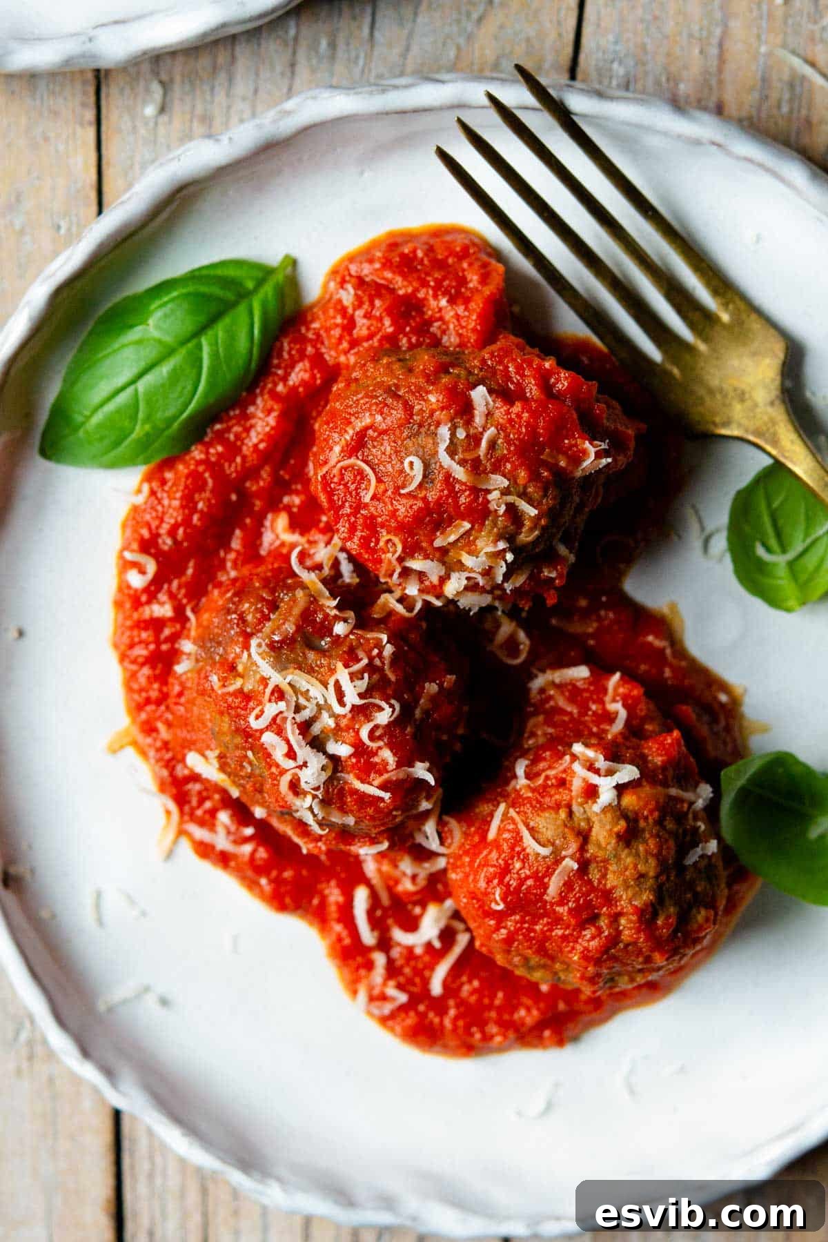 An overhead close up of three Italian meatballs on a plate with tomato sauce and basil leaves