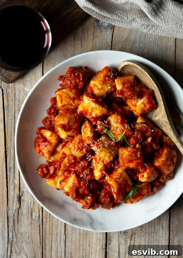 An overhead shot showcasing a large white bowl filled with sausage ragu generously tossed with homemade ricotta gnocchi, ready to be enjoyed.